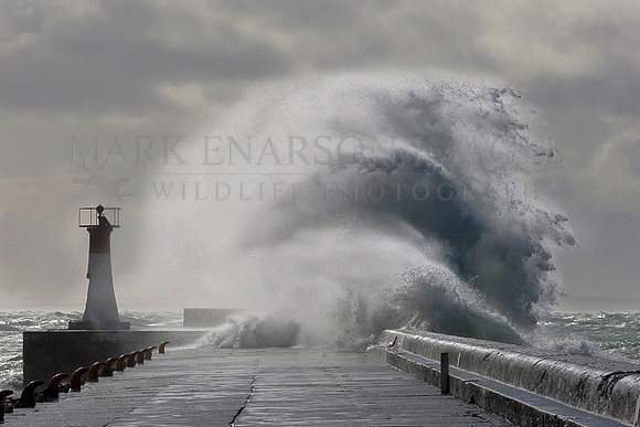 Waves crash over the lighthouse at Kalk Bay harbor, False Bay, South Africa