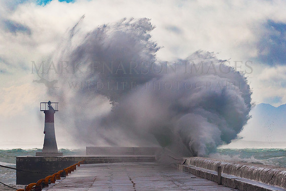 Waves crash over the lighthouse at Kalk Bay harbor, False Bay, South Africa